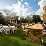 Long wooden farm table and white chairs on a resort lawn