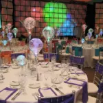 Corporate dinner with glowing bulb centerpieces and a lit video wall backdrop