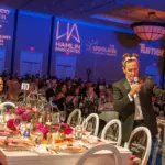 Charity gala ballroom with long banquet tables, blue uplighting and a guest speaker