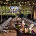 Long banquet table under hanging lights in a greenhouse-style corporate dinner