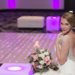 Bride posing on a purple LED dance floor with lounge furniture