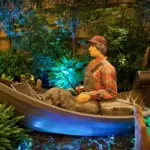 Fisherman figure in a boat among tropical plants with teal lighting