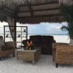 Wicker lounge seating under a thatched cabana on the beach