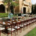 Long banquet table with Chiavari chairs beside a courtyard water feature